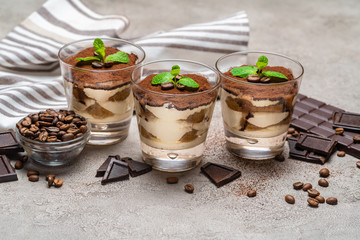 Classic tiramisu dessert in a glass cup and pieces of chocolate bar on concrete background