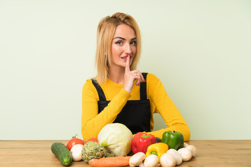 Young blonde woman with lots of vegetables doing silence gesture