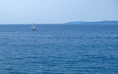 Obraz premium Single white boat sailing on calm water, along the coast of the Mediterranean on the background of the islands. Water activities, vacation at sea, happy holidays in the sea.