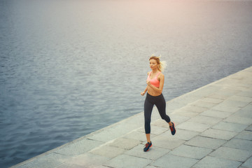 Just running. Full length of young and active blonde woman in sports clothing running along the riverbank in the morning