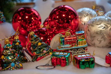 Christmas gifts and decorations. Traditional glass Christmas ornaments in shapes of Christmas tree and red train closeup with blurry red and white balls on background. Holiday fair in Berlin Germany. 