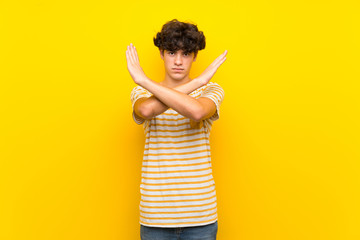 Young man over isolated yellow wall making NO gesture