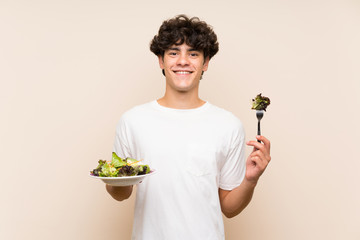 Young man with salad over isolated green wall