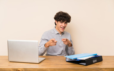 Young student man with a laptop pointing to the front and smiling