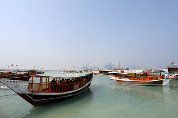 Fototapeta na wymiar Doha / Qatar – October 10, 2018: Traditional dhows moored up along the corniche in the Qatari capital Doha, with the skyscrapers of the West Bay area in the background