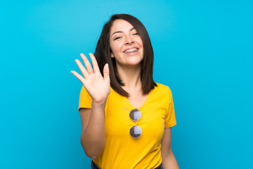 Young Mexican woman over isolated blue background saluting with hand with happy expression