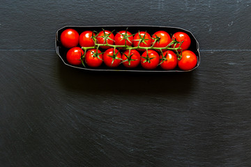Red cherry tomatoes on dark background with copy space – Organic and fresh vegetables for a heathy lifestyle in paper tray – Vegan food full of vitamins and nutrients