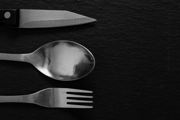 Shiny silverware placed on the left side on a black background with copy space – Kitchen stainless steel tools on stone textured surface