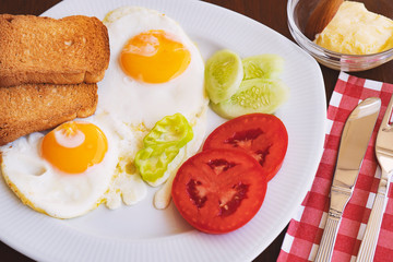 Breakfast - fried eggs, butter and tomato in white plate. Close up image