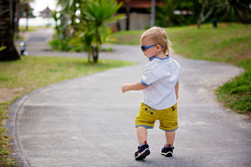 Adorable fashion baby toddler boy, dressed in casual clothes, walking in a beautiful resort gardens