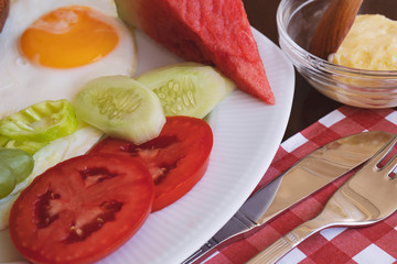 Breakfast - fried eggs, butter and tomato in white plate. Close up image