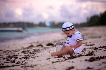 Beautiful toddler boy, dressed as a sailor, playing on the beach on sunset, enjoying tropical magical holiday vacation