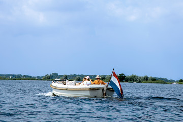Tourists enjoying ride in white luxury motor boat with dutch flag. Summer vacation or boat rent theme.