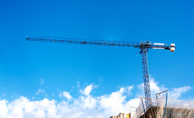 a crane lifting weights on a construction site with a blue sky and clouds on the background.
