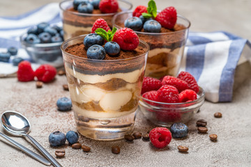 Classic tiramisu dessert with blueberries and raspberries in a glass and napkin on concrete background
