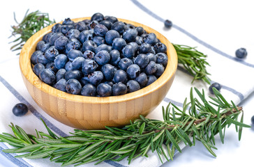 Many blueberries in a wooden bowl placed on the fabric.