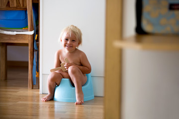 Little toddler boy, sitting on potty, playing with wooden toy