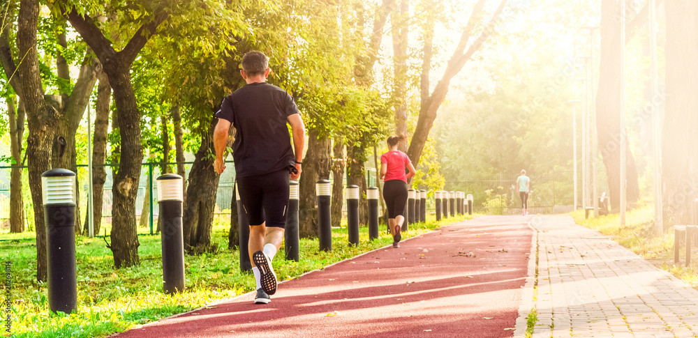 Wall mural back view of people runner running on the road against the sun light. people jogging in the park in 