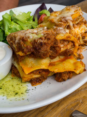 Tomato and beef lasagne with cheese layered between sheets of traditional Italian pasta served on a white plate on a restaurant or bar