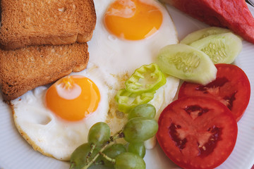 Breakfast - fried eggs, butter and tomato in white plate. Close up image
