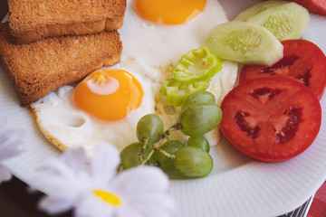 Breakfast - fried eggs, butter and tomato in white plate. Close up image