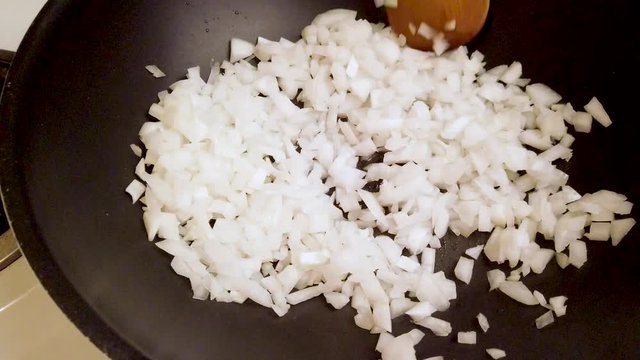 A Chef Stirring Raw Onions Around A Black Frying Pan On A Stove Top In The Kitchen Tight Overhead.