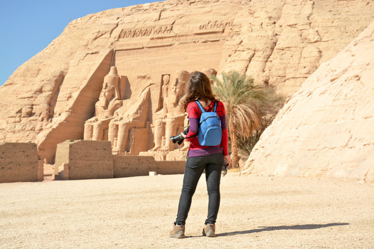 Young woman in a casual dress taking photos of the famous Abu Simbel temple in Egypt on a sunny day.