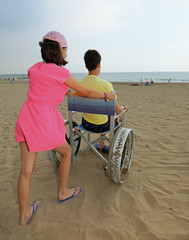 little girl moves the wheelchair on the beach with a young boy