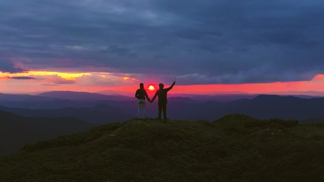 The couple with a firework stick standing on a mountain with a beautiful sunrise