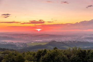 Sunset with view on landscape with fully colored clouds and orange sun goes down and city Valasske Mezirici captured during summer late time