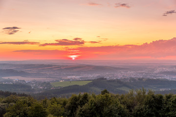 Sunset with view on landscape with fully colored clouds and orange sun goes down and city Valasske Mezirici captured during summer late time