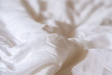 Fototapeta na wymiar Shallow Depth of Field Closeup of Wrinkled White Cotton Bedsheets with Natural Light Shining onto them in the Morning