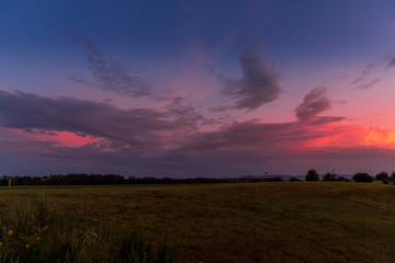 Naklejka na ściany i meble Landscape sunset with fully colored clouds pink orange sky look on meadow close to city Valasske Mezirici captured during summer late time.