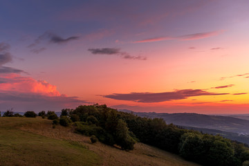Naklejka na ściany i meble Landscape sunset with fully colored clouds pink orange sky look on meadow close to city Valasske Mezirici captured during summer late time.