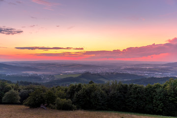 Landscape sunset with fully colored clouds pink orange sky look on meadow close to city Valasske Mezirici captured during summer late time.
