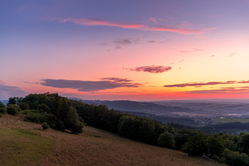 Landscape sunset with fully colored clouds pink orange sky look on meadow close to city Valasske Mezirici captured during summer late time.
