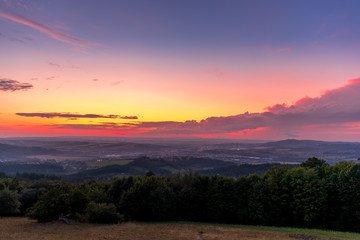 Landscape sunset with fully colored clouds pink orange sky look on meadow close to city Valasske Mezirici captured during summer late time.