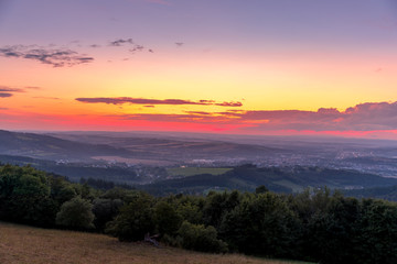 Landscape sunset with fully colored clouds pink orange sky look on meadow close to city Valasske Mezirici captured during summer late time.