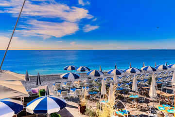 Vue sur la plage de Nice   La France, avec parasols, transats, mer bleue et soleil.