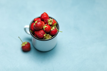 Strawberries in white enamel mug on a blue background