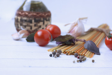 spaghetti, bazil, peppercorn garlic, cherry tomatoes and a bottle of oil on white wooden background