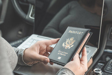 Woman in the car with laptop and american passport. Travel concept.