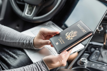 Woman in the car with laptop and american passport. Travel concept.