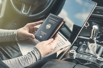 Woman in the car with laptop and germany passport. Travel concept.