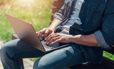Naklejka premium Close up view of multicultural businessman siting on a bench and working with his laptop