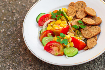 salad with vegetables and crackers (tomato, cucumber, breadcrumbs, corn, salad dressing). food background. top view, copy space