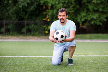 Portrait of a footbal trainer or gym teacher standing on one knee holding and giving soccer ball to...