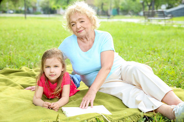 Naklejka na ściany i meble Cute little girl with grandmother resting in park