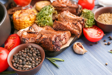 Tasty grilled meat with spices and vegetables on wooden background