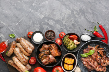 Tasty grilled meat with sausages and vegetables on grey background